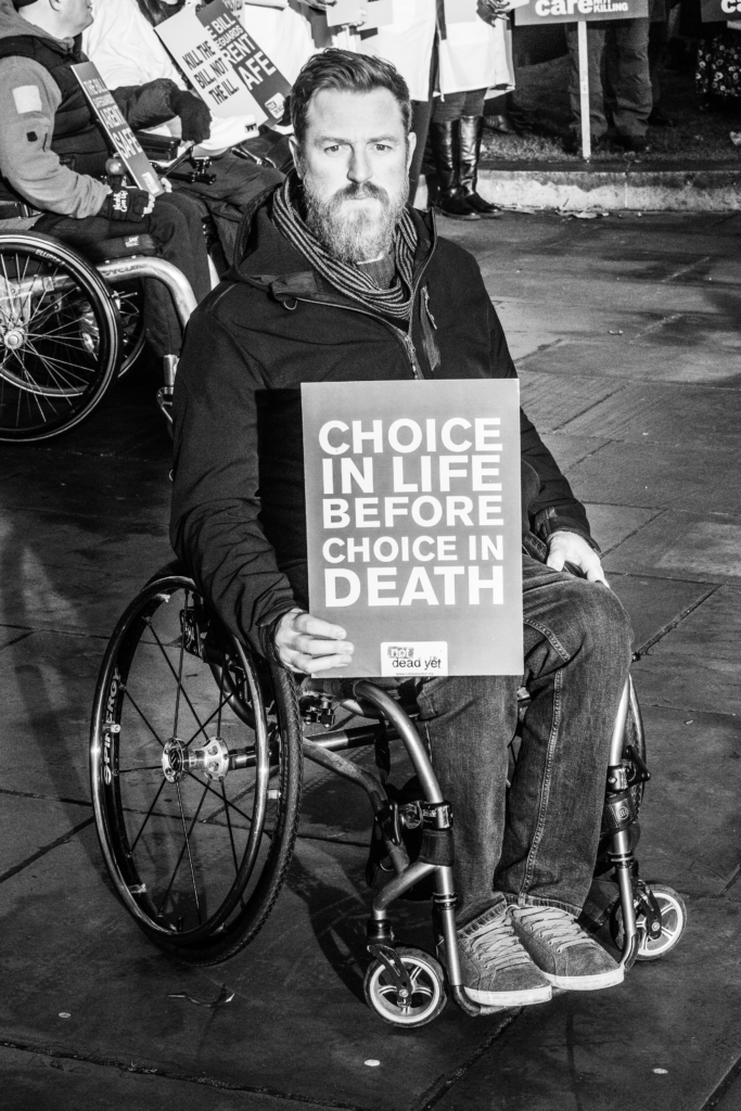 Wheelchair user holding sign "Choice in life before choice in death"